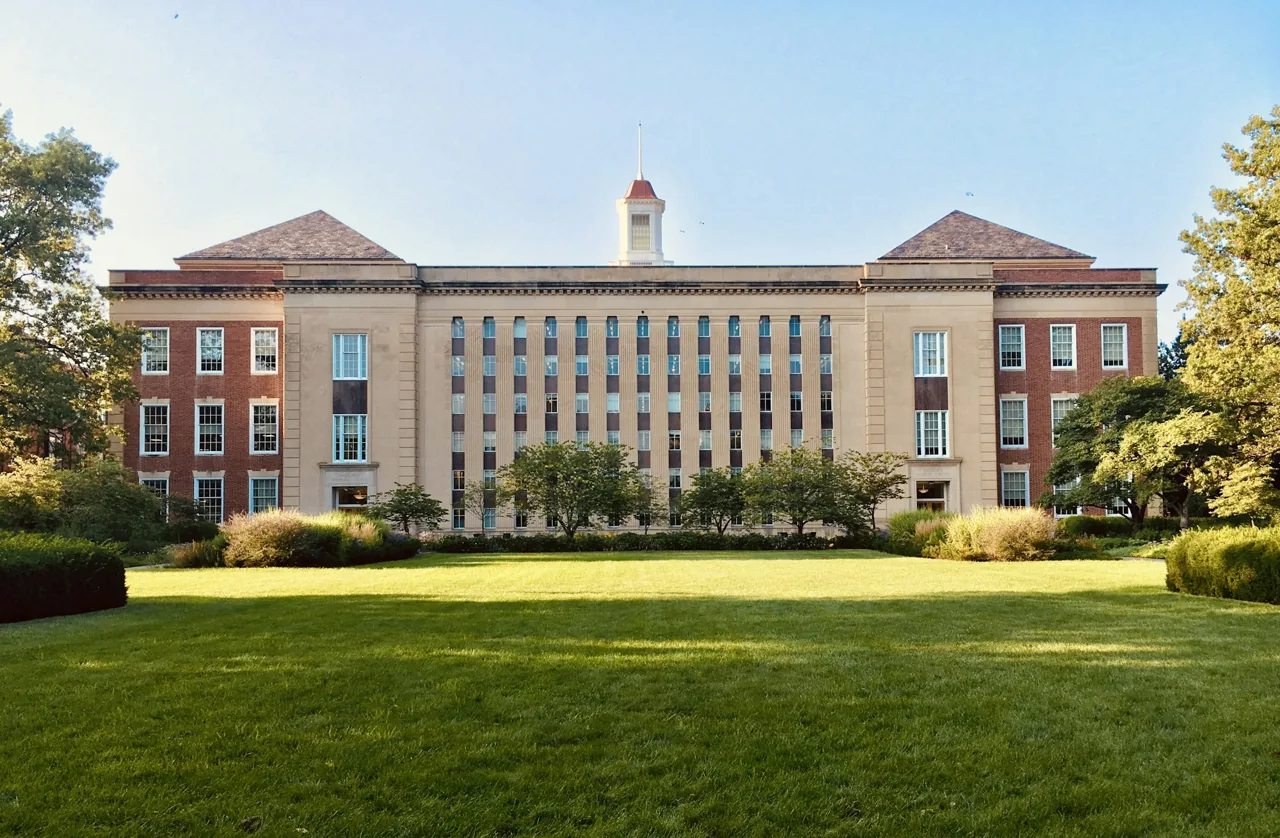 A stately academic building surrounded by green lawns and trees.